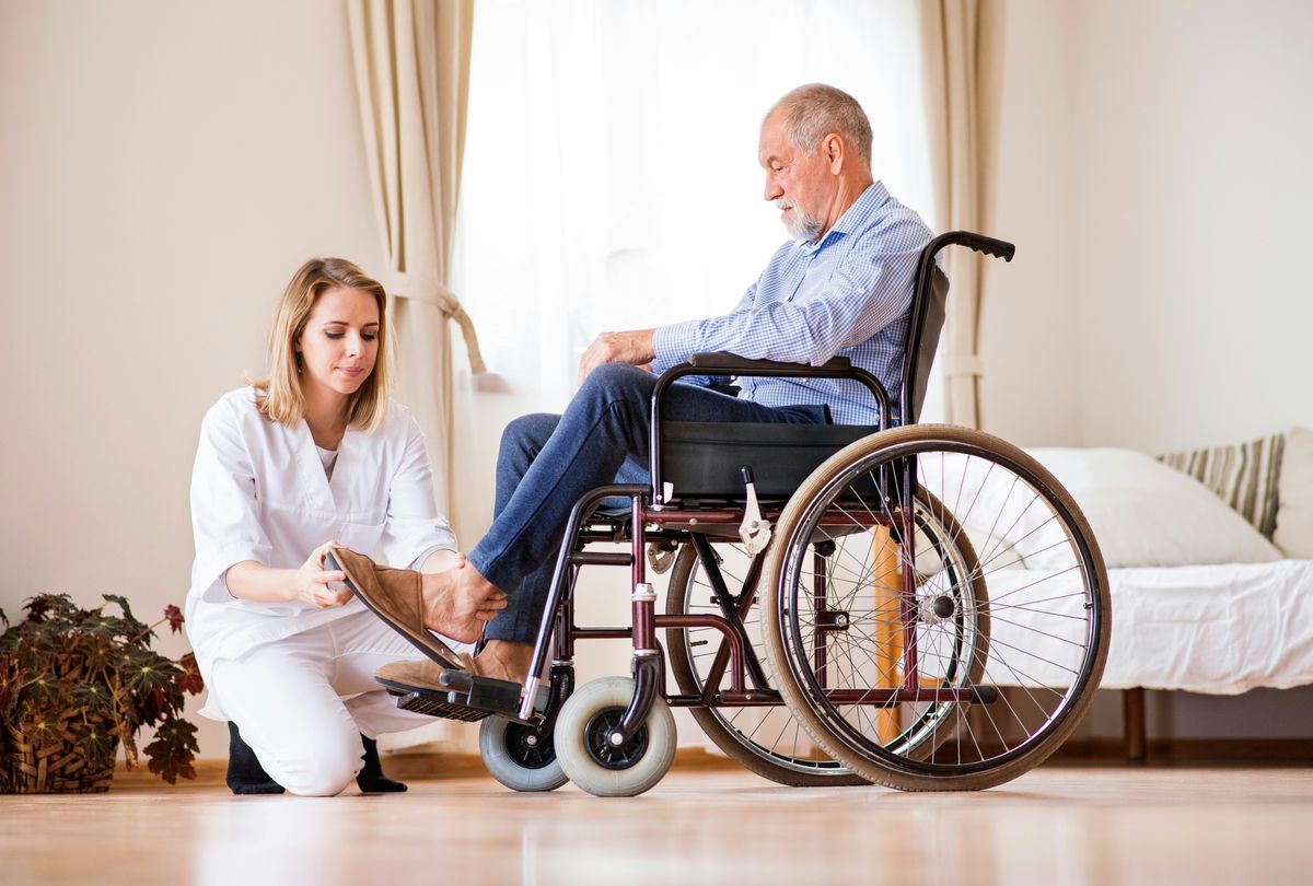 Assistant helping elderly man put his shoe on