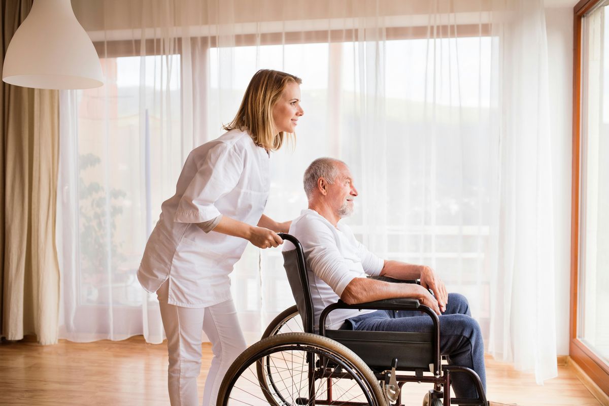 Assistant helping push elderly man in his wheelchair