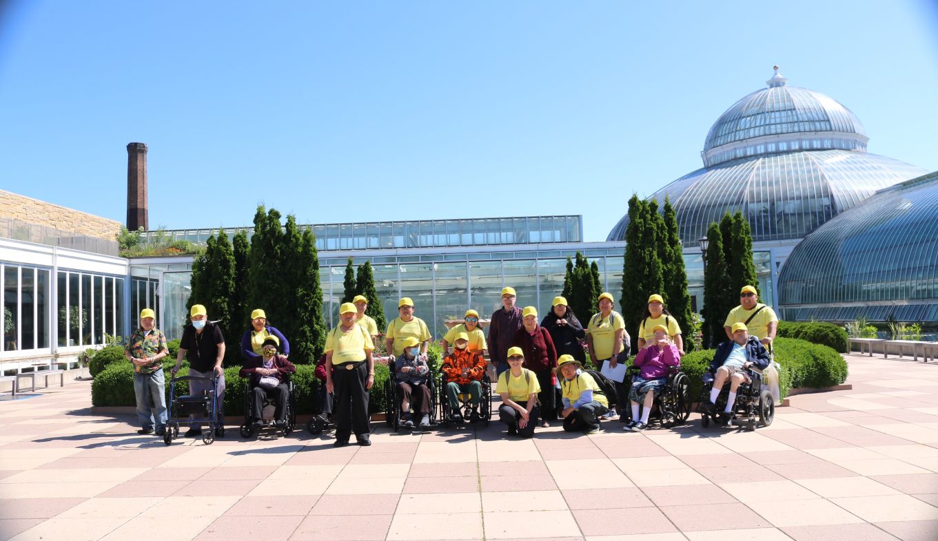 Residents and staff in matching yellow caps on a group outing at a glass conservatory